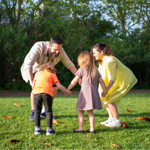 Family of 4, mom and dad playing outside with younger son and daughter holding hands.